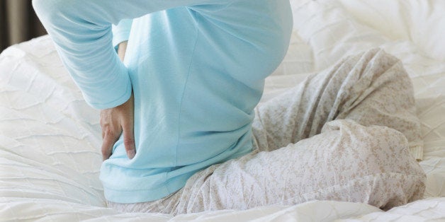 Profile of a mature woman holding her lower back gingerly while sitting on her bed