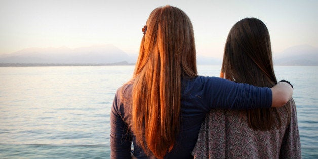 Standing women hugging each other and looking away.