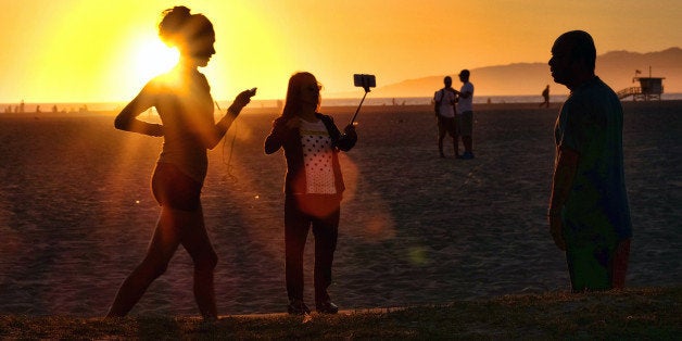 In this Friday, March 27, 2015 photo, a beachgoer using a cell phone on a stick snaps a selfie as the sun sets at Venice beach in Los Angeles. You can bring your beach towels and floral headbands, but forget that selfie stick if youᅢ까タᅡルre going to the Coachella or Lollapalooza music festivals. The sticks are banned this year at the events in Indio, California, and Chicago. Coachella dismissed them as ᅢ까タᅡワnarsissticsᅢ까タᅡン on a list of prohibited items. (AP Photo/Richard Vogel)