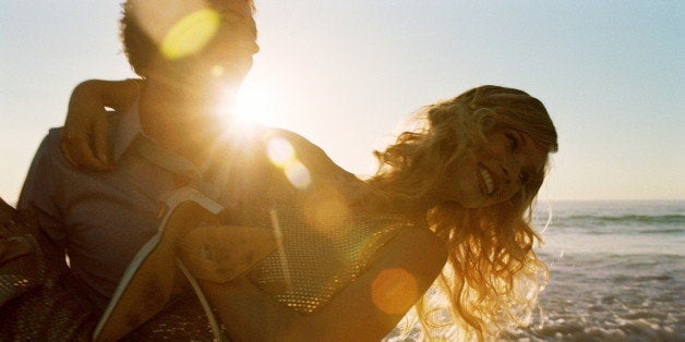 Young couple on beach at sunset, man carrying woman in arms