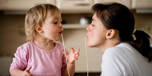 Mother and her little child sucking together spaghetti noodles.