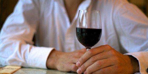 An unidentified man sits at a restaurant table drinking red wine.