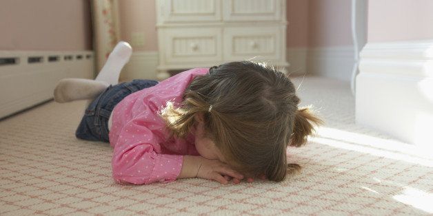 Young girl laying on bedroom carpet covering face