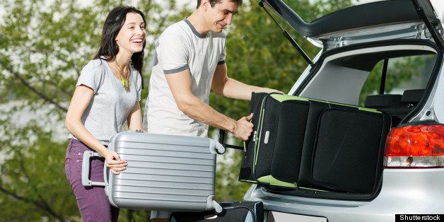 Happy couple going to vacations, loading their car boot with travel suitcases
