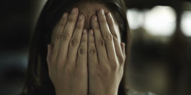 A young woman looking anxious and fearful with her hands over her eyes