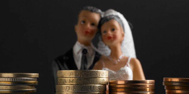 Bride and groom wedding figure standing in front of a stack of pound coins (Concept of the cost of weddings/pre nutual agreement)