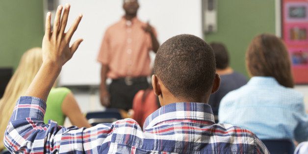 Male Pupil Raising Hand In Class Sitting At Desk