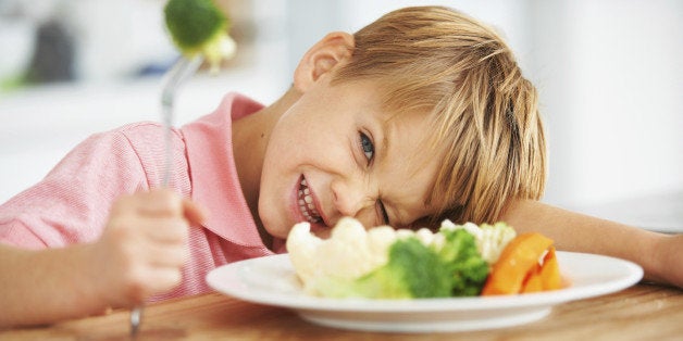 Portrait of a cute young boy looking naughty while holding a piece of broccoli on his fork