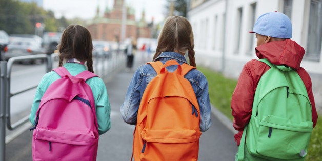 Backs of schoolkids with colorful rucksacks moving in the street