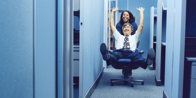 Co-workers racing through cubicles with office chair.