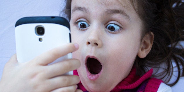 Portrait of a shocked little girl looking at phone. Horizontal composition. Image developed from Raw format. Little girl looking at phone and gesturing shock.