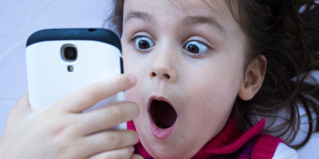 Portrait of a shocked little girl looking at phone. Horizontal composition. Image developed from Raw format. Little girl looking at phone and gesturing shock. 