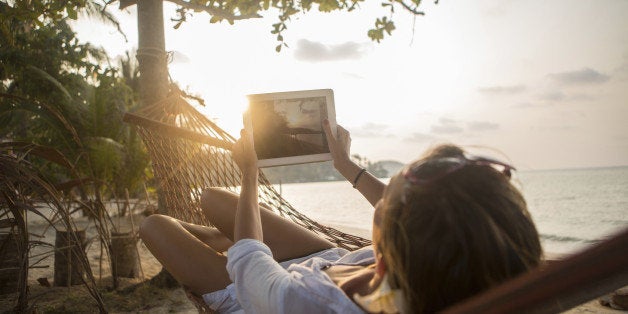 Young attractive woman taking a picture of the sunset with her digital tablet.