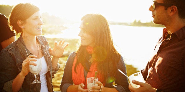 Group of three friends standing on dock at sunset eating dessert and talking