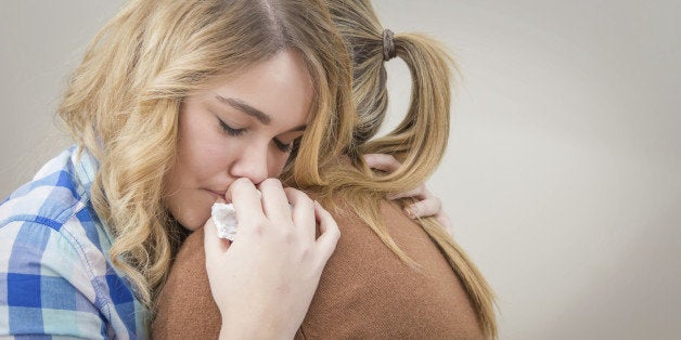 Closeup on sad teen daughter crying by problems in the shoulder of her mother. Mother embracing and consoling daughter.