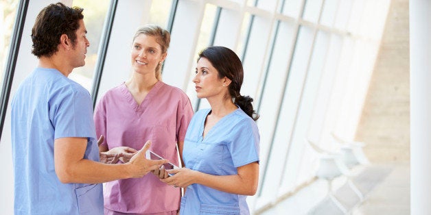 Medical Staff Talking In Hospital Corridor With Digital Tablet