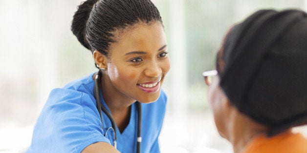 caring african medical nurse comforting senior patient in office