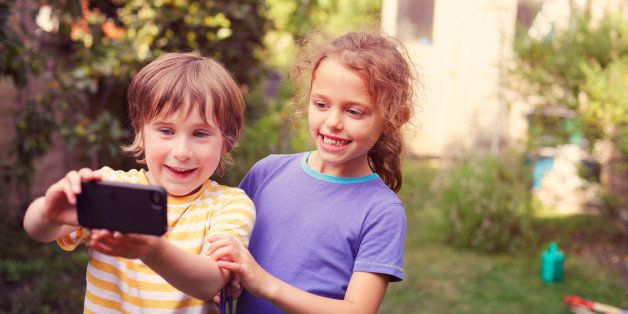 A young boy taking a picture of himself and his friend with a smartphone in a sunny garden.