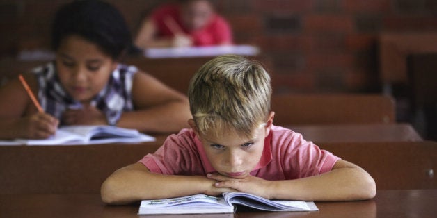 A young boy resting his head on his arms as he sits in a classroom looking bored