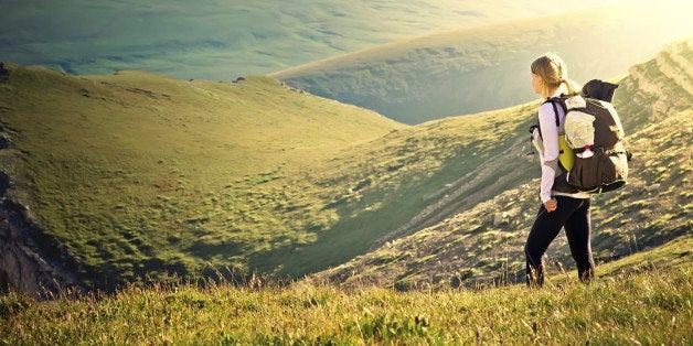 Woman with backpack hiking in mountains, spending summer vacation