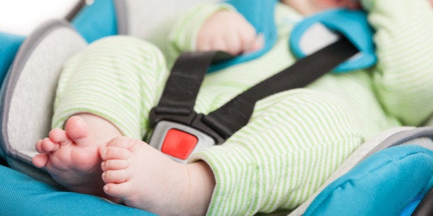 Little smiling baby child fastened with security belt in safety car seat