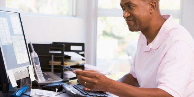 Man in home office using computer holding credit card and smiling