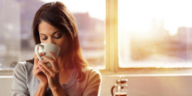 Woman drinking coffee at home with sunrise streaming in through window and creating flare into the lens.