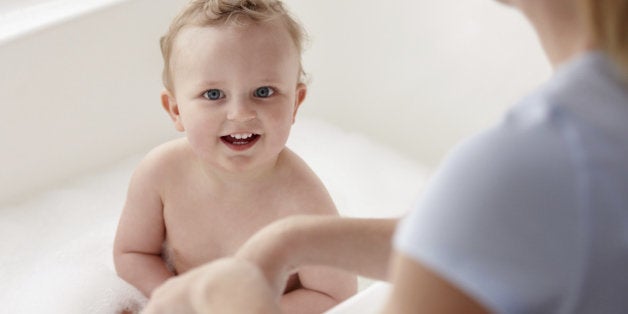 A baby in a bath tub with his mother watching over him