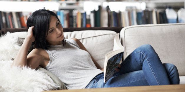 Woman relaxing on sofa reading a book in her cozy loft apartment
