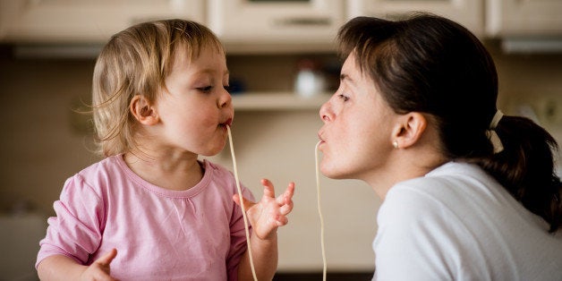 Mother and her little child sucking together spaghetti noodles.