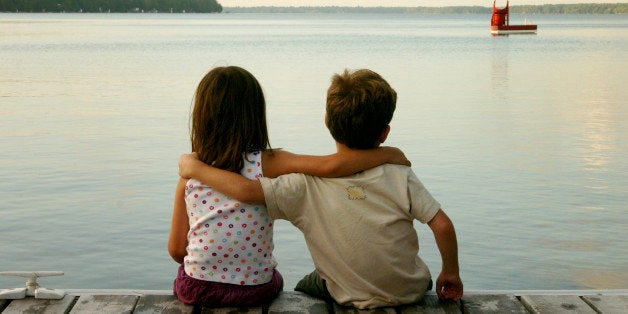 Boy and girl sitting on dock front of sea.