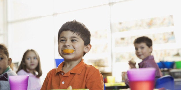 Playful boy holding orange slice in mouth at school at snack time