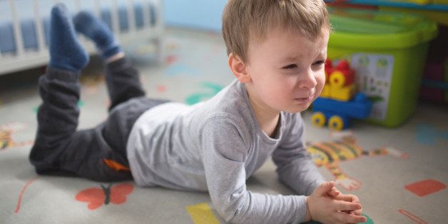 Toddler in his 'terrible twos' lying on the floor of his room, making a sad face and whining