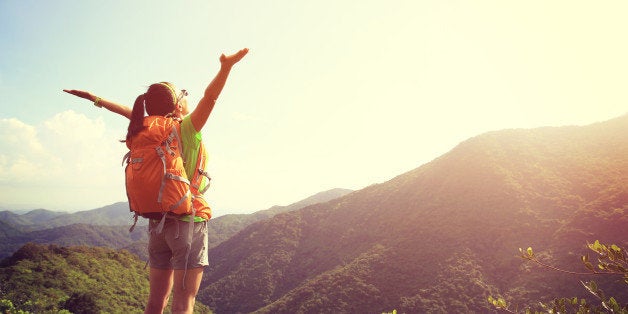 cheering woman hiker open arms at mountain peak cliff