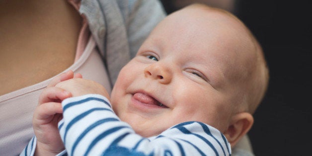 2 months old baby boy portrait. He is in mother's hands, he is looking at camera, smiling. He is sticking out his tongue.