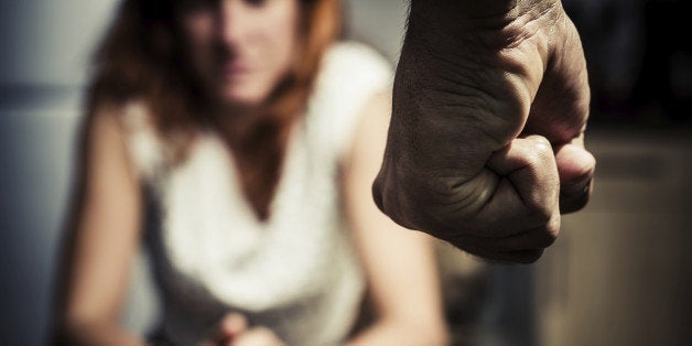 Young woman is sitting hunched at a table at home, the focus is on a man's fist in the foregound of the image