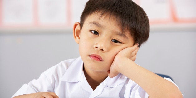 Unhappy Male Student Working At Desk In Chinese School Classroom