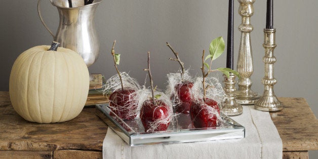 A platter of candied apples with spun sugar, candles, a white pumpkin and decorations for a Halloween Party