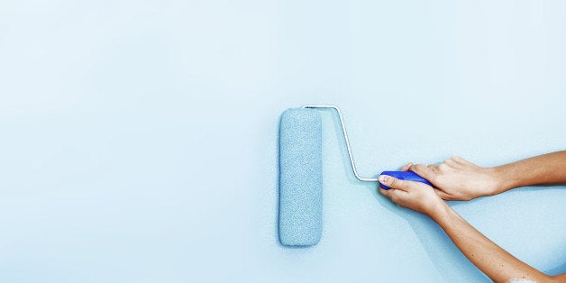 Hands painting the wall with a roller brush