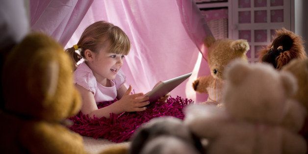 little girl reads a story to all her teddies from a digital tablet.**main teddy in focus is non branded pre-1970**