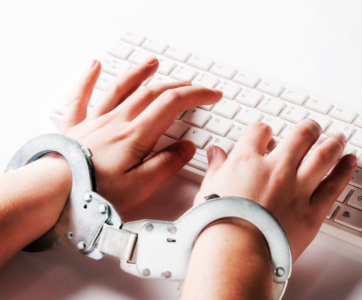 Young woman's handcuffed hands typing on computer keyboard