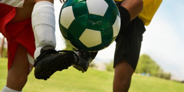 Two little league players (7-9 years) kicking ball mid air, mid section, close up