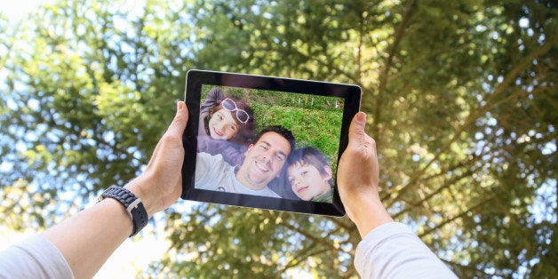 Man with his two nephews taking a funny selfie laying face up on the backyard grass from personal point of view on a sunny spring day.