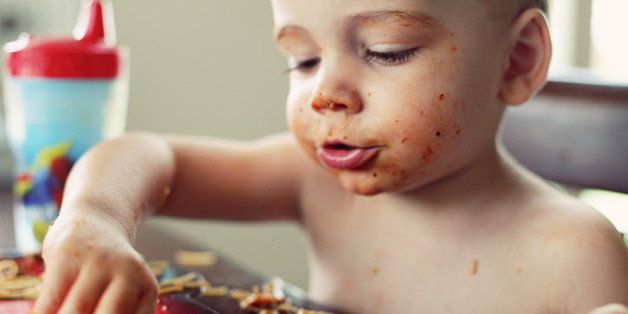 Spaghetti sauce on boy's face. Food on table and plate.