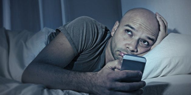 young cell phone addict man awake at night in bed using smartphone for chatting, flirting and sending text message in internet addiction and mobile abuse concept