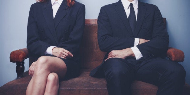 Two sharply dressed business people are waiting on a sofa with a serious expression on their faces. Maybe they're waiting to enter a job interview, or maybe they're a couple waitng to see a divorce lawyer