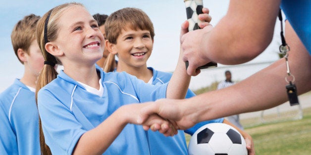 Happy little girl shaking hands with soccer coach receiving trophy. 