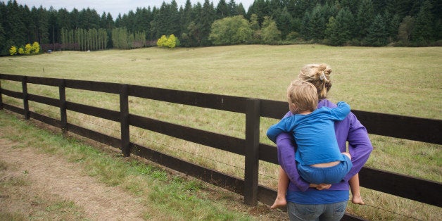 Woman carries son along wooden fence.