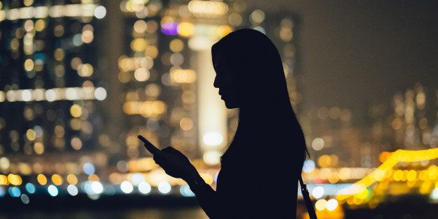 Silhouette of young woman with smartphone against the spectacular night scene of urban city.