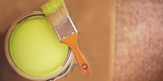 Green paint bucket with paint brush on cardboard.